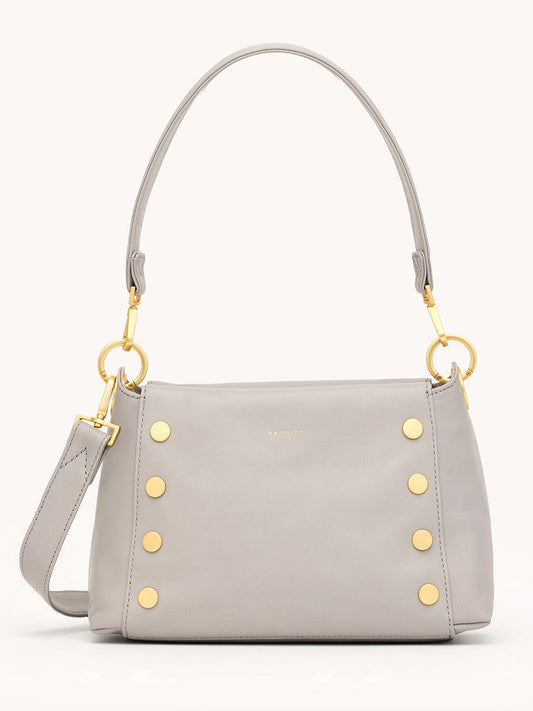 The Hammitt Los Angeles Bryant Medium Crossbody Bag in Stormy/Brushed Gold features light gray pebbled leather, gold studs, a detachable strap, and a short handle, shown against a plain background.