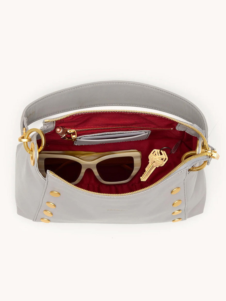 A Hammitt Los Angeles Bryant Medium Crossbody Bag in Stormy/Brushed Gold, open to show a red interior with sunglasses, a key, and a small zipped pocket.