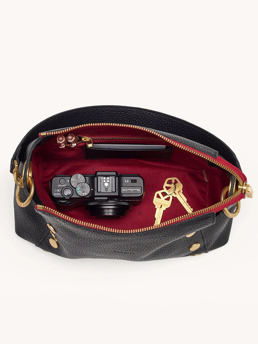 The Hammitt Los Angeles Bryant Medium Crossbody Bag in Black is a chic pebbled leather crossbody bag featuring a striking red interior, ideal for carrying your everyday essentials like a camera, keys, and lipstick.