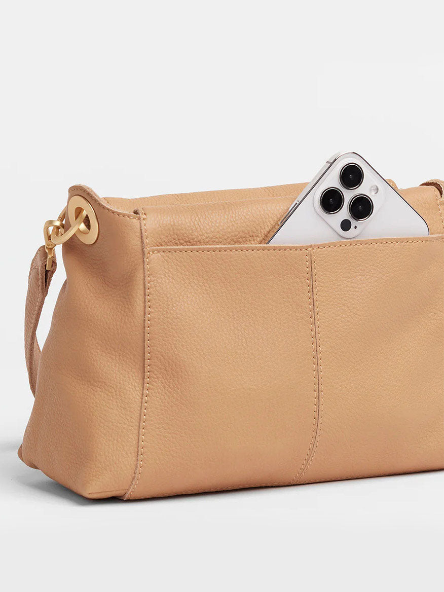 The Hammitt Los Angeles Bryant Medium Crossbody Bag in Toast Tan, a beige crossbody and shoulder bag with pebbled tan leather, displays a smartphone partially visible in its outer pocket.