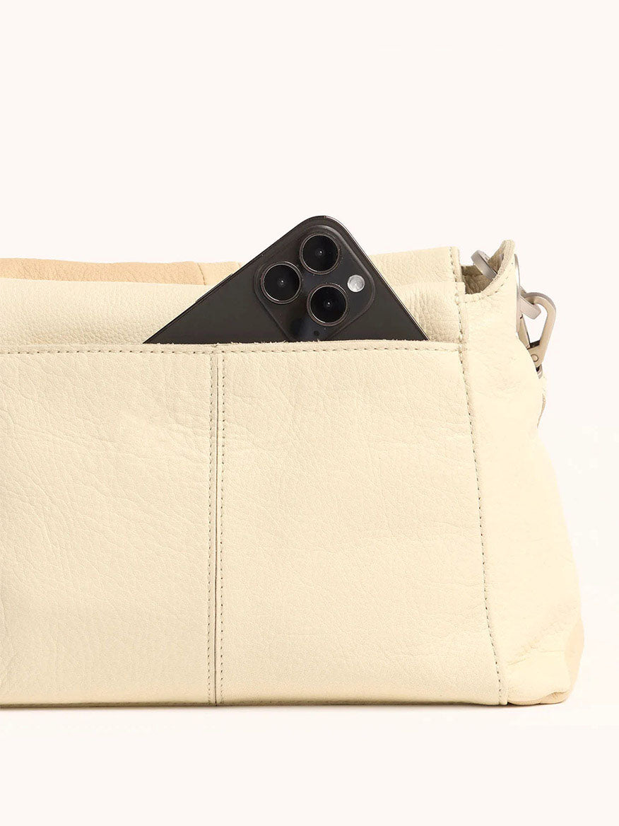 A smartphone peeks from the outer pocket of a Hammitt Los Angeles Bryant Medium Crossbody Bag in Coastal Cream, highlighting its chic design.