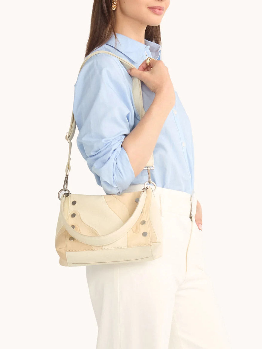 A person in a light blue shirt and white pants carries the Hammitt Los Angeles Bryant Medium Crossbody Bag in Coastal Cream over their shoulder.