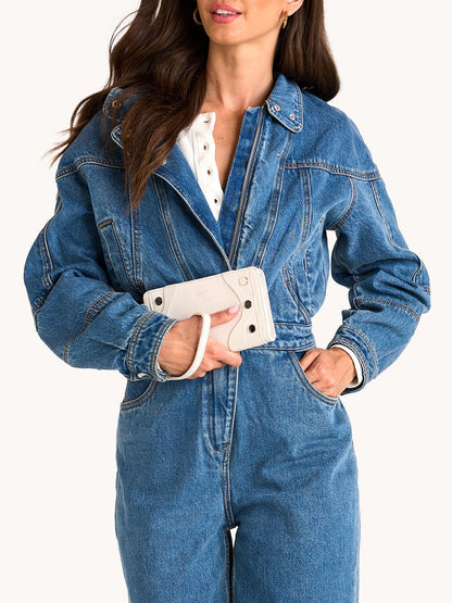 Woman wearing a blue denim jacket and jeans, holding the Hammitt Los Angeles Bryant Wallet in Western Rein/Silver, crafted from pebble leather with a sleek hand strap and detachable wristlet for versatile style.
