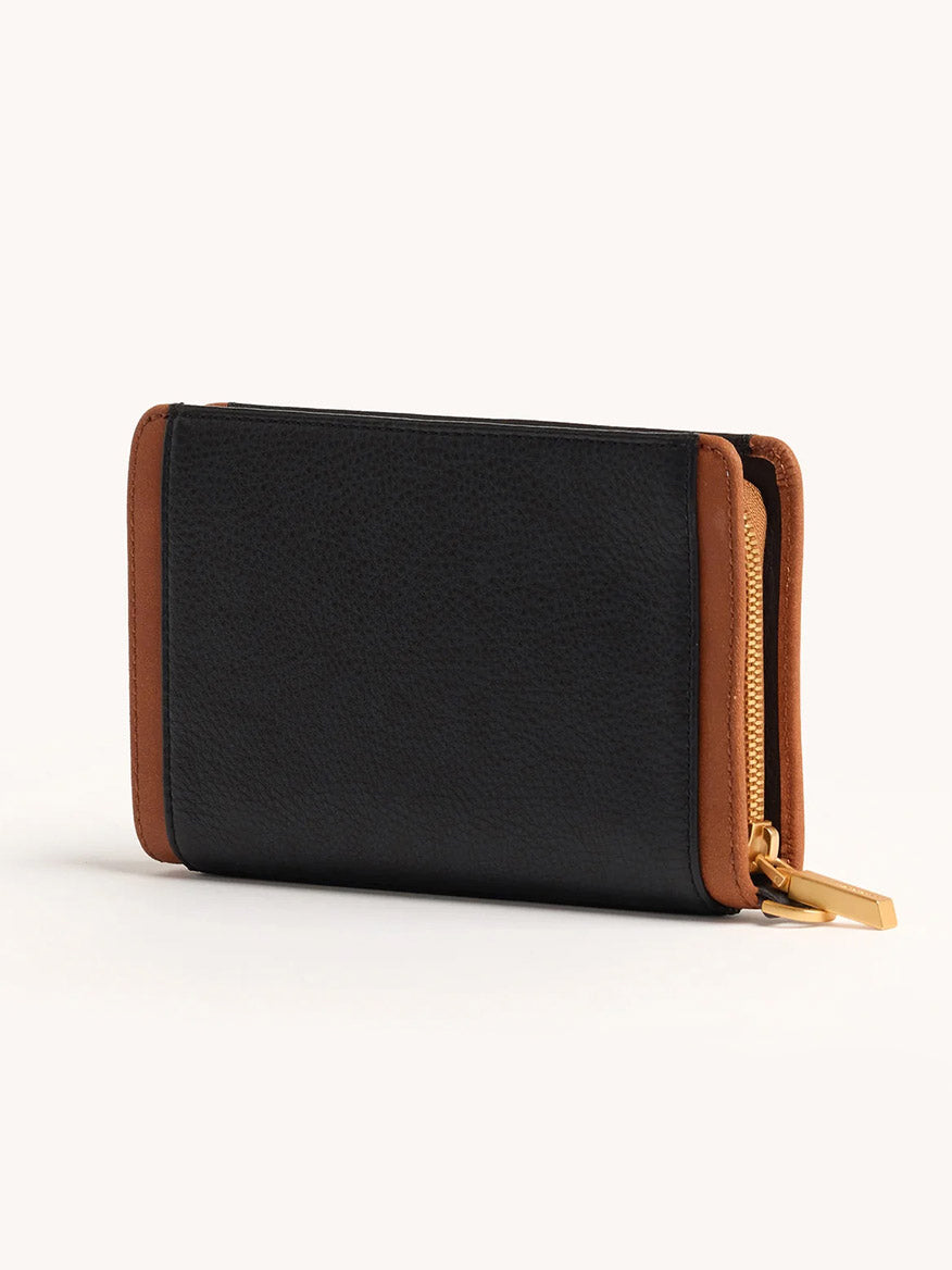 A Hammitt Los Angeles Bryant Wallet in North End, small and black with brown edges and a gold zipper, is displayed closed and standing upright on a light background.