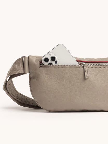 A Hammitt Los Angeles Charles Crossbody Large in Pewter Pebble/Brushed Silver with a zippered pocket, partially unzipped to reveal a smartphone inside.