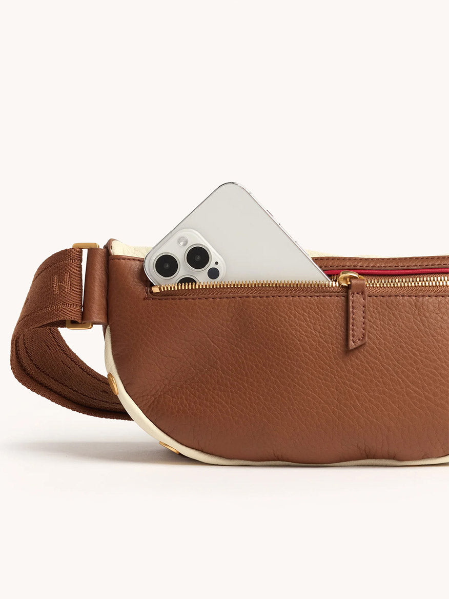 Hammitt Los Angeles Charles Crossbody Medium in Courtyard Cream with a visible gold zipper, partially open to reveal a white smartphone inside the main compartment, photographed against a plain background.