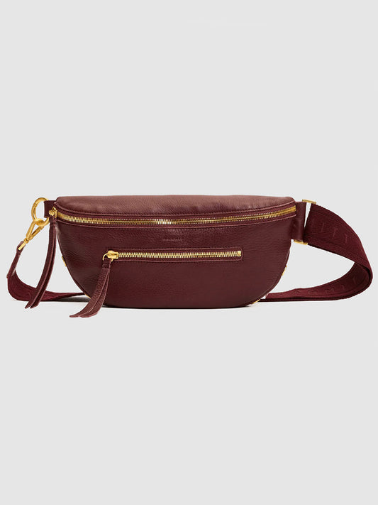 Featured against a plain light background, the Hammitt Los Angeles Charles Crossbody Medium in Cherrywood Pebble/Brushed Gold showcases maroon pebble leather, gold zippers, a front pocket, and an adjustable strap.