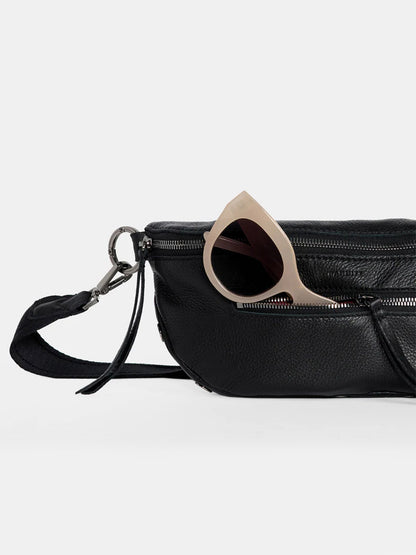 A stylish Hammitt Los Angeles Charles Crossbody Medium in Black/Gunmetal, featuring a zippered pocket partially open to reveal a pair of beige sunglasses.