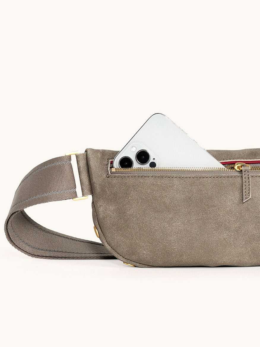 A Hammitt Los Angeles Charles Crossbody Medium in Pewter Brushed Nubuck/Brushed Gold, with a smartphone partially visible inside its zippered pocket, shown against a plain background.