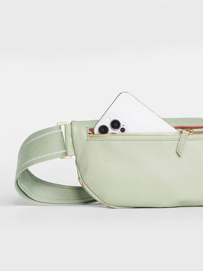 A Hammitt Los Angeles Charles Crossbody Medium in Cypress Sage with a white card peeking out, resembling eyes, creating a playful face-like appearance.