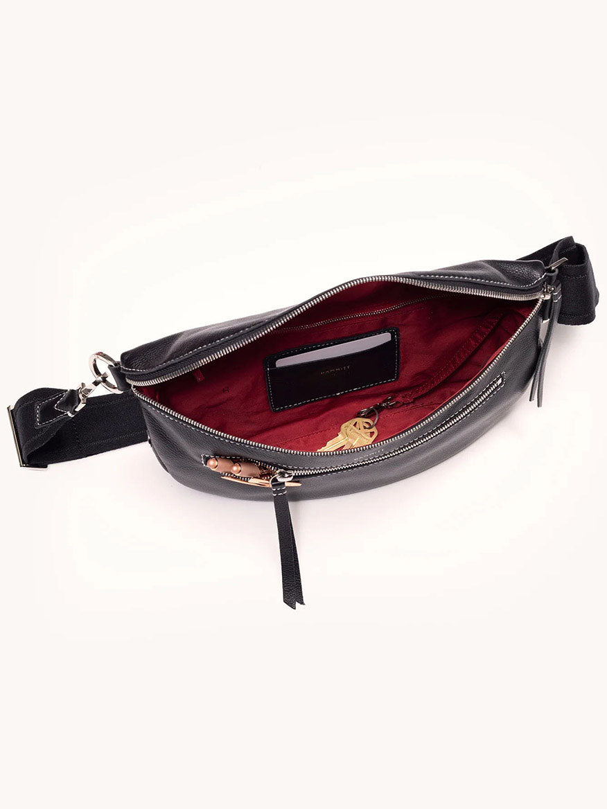 The Hammitt Los Angeles Charles Crossbody Large in Tempo Black is a black pebbled leather belt bag with a red interior lining, silver hardware, two zippers, an adjustable strap for crossbody wear, and an inside pocket.