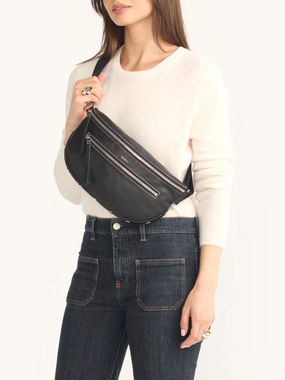 A person in a white sweater and dark jeans carries a Hammitt Los Angeles Charles Crossbody Large in Tempo Black, featuring an adjustable strap over their shoulder.