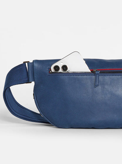 A Hammitt Los Angeles Charles Crossbody Large in Vintage Navy bag with a white smartphone peeking out from an unzipped compartment.