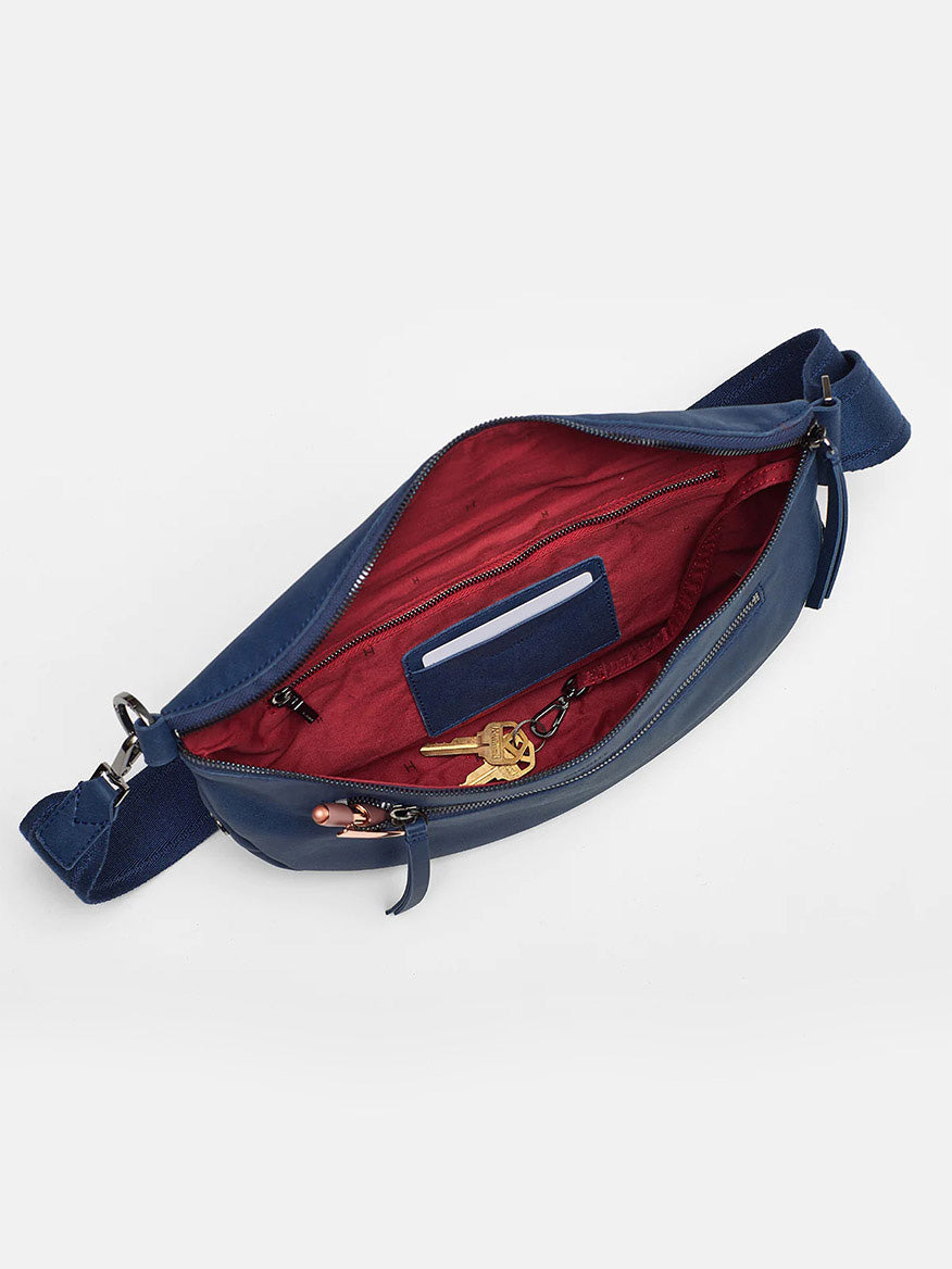 A Hammitt Los Angeles Charles Crossbody Large in Vintage Navy unzipped to show a red interior with a mobile phone and keys inside, against a white background.