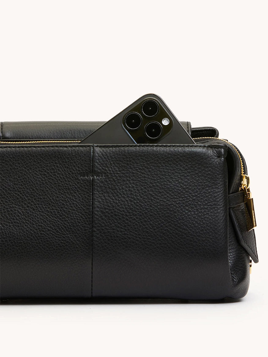A black smartphone is partially tucked into the exterior pocket of the Hammitt Los Angeles Charlotte Medium in Black/Gold.