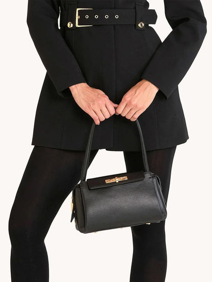 A person in a black belted coat and tights holds the Hammitt Los Angeles Charlotte Medium handbag in Black/Brushed Gold with gold hardware.