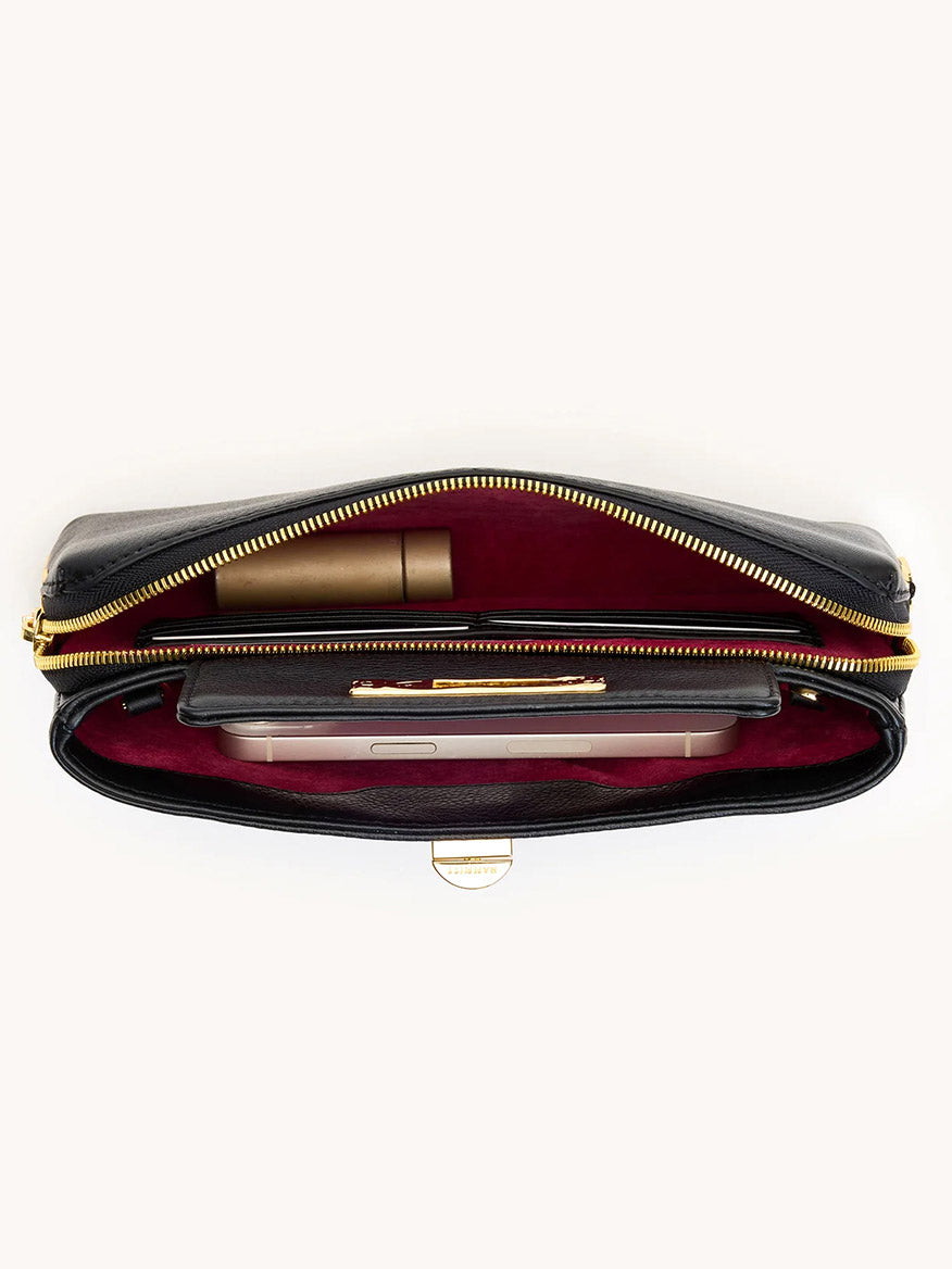 The Hammitt Los Angeles Charlotte Small in Black/Gold is an open black pebble leather zippered pouch with a red interior, neatly storing a smartphone, pen, and cylindrical item—ideal as a wallet-on-chain or compact crossbody bag.