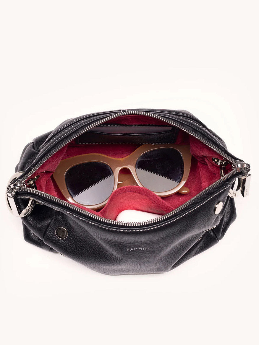 A Hammitt Los Angeles Daniel Crossbody Clutch Small in Tempo Black displays wooden sunglasses against a red lining with its zipper open.