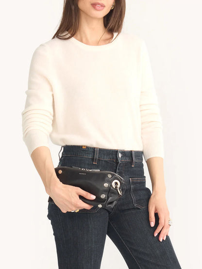 A woman in a white sweater and dark jeans holds the chic Hammitt Los Angeles Daniel Crossbody Clutch Small in Tempo Black, highlighting its sleek design.