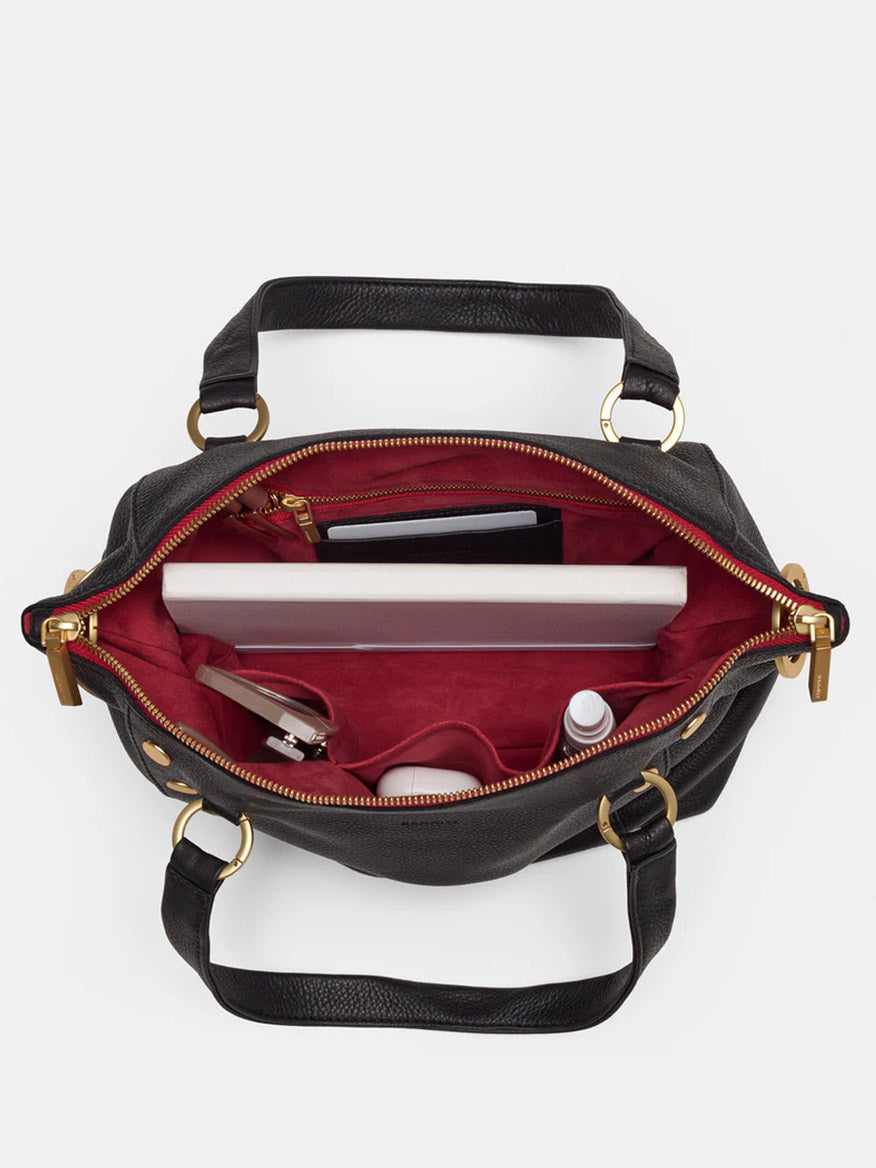 The Hammitt Los Angeles Daniel Medium Satchel in Black with Brushed Gold and Red Zip is a classic black leather handbag that opens to reveal a red interior, perfect for holding essentials like a laptop, sunglasses, a wallet, and a small bottle. The adjustable crossbody strap adds versatility to this timeless accessory.