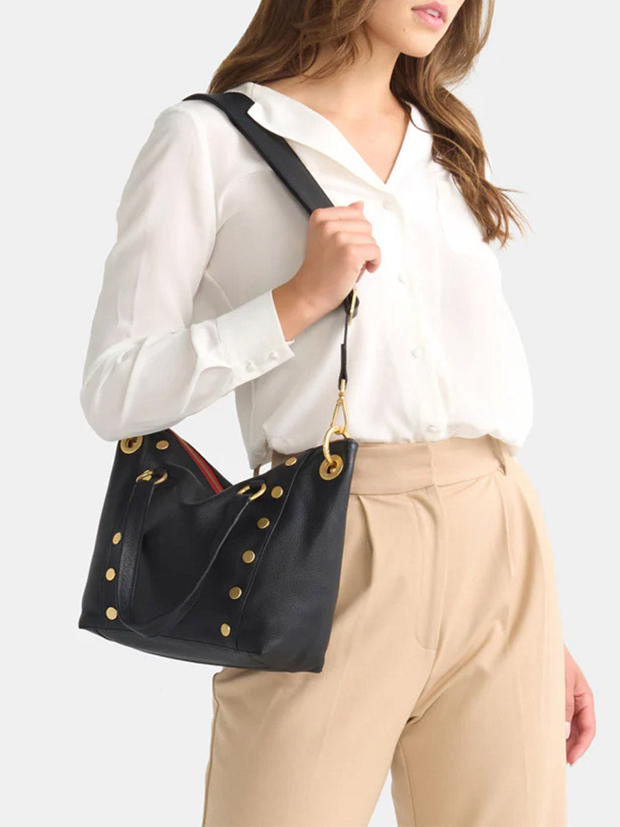 Woman wearing a white blouse and beige pants, holding a Hammitt Los Angeles Daniel Medium Satchel in Black with Brushed Gold and Red Zip.