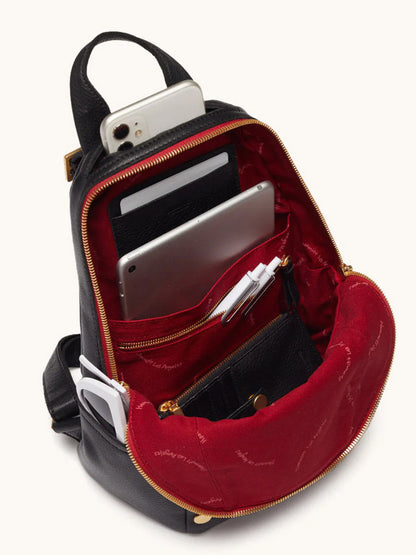 The Hammitt Los Angeles Hunter Medium Backpack in Black/Brushed Gold/Red Zip is unzipped, revealing a neatly organized phone, tablet, wallet, pens, and other small items inside its vibrant red interior.