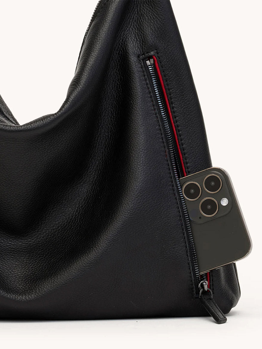 A black/gunmetal Hammitt Los Angeles Kyle Large Shoulder Bag features a partially open zipper pocket with a smartphone inside, highlighting its stylish and practical design.