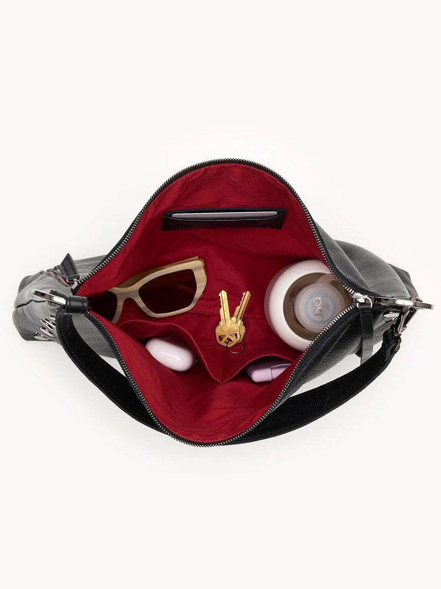 Open the Hammitt Los Angeles Kyle Large Shoulder Bag in Black/Gunmetal, revealing a red interior with sunglasses, a water bottle, lipstick, a compact mirror, and a keychain shaped like a hand making a peace sign inside.
