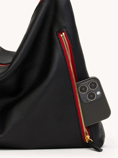 The Hammitt Los Angeles Kyle Large Shoulder Bag in Black with brushed gold hardware and a red zip is shown partially open, revealing a smartphone inside its front pocket.