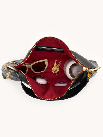 The Hammitt Los Angeles Kyle Large Shoulder Bag in Black/Brushed Gold & Red Zip displays sunglasses, a keychain, two round containers, and a bottle inside its spacious red-lined interior.