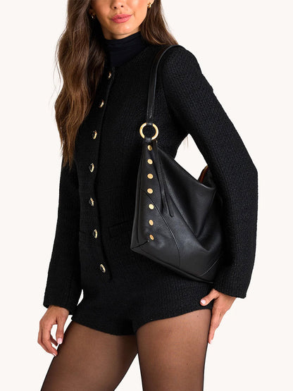 A woman in a black buttoned long-sleeve outfit and sheer tights carries the Hammitt Los Angeles Kyle Large Shoulder Bag in Black/Brushed Gold & Red Zip.