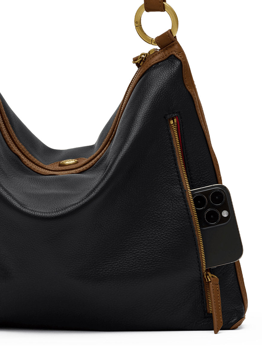 A stylish Hammitt Los Angeles Kyle Large Shoulder Bag in East End/Antique Gold, crafted from black pebbled leather with brown trim and gold hardware, featuring a zippered side pocket partially open with a smartphone inside.