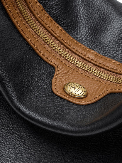 Close-up of a Hammitt Los Angeles Kyle Large Shoulder Bag in East End/Antique Gold, featuring black pebbled leather with brown trim, a gold zipper, and a round gold emblem with an abstract design.