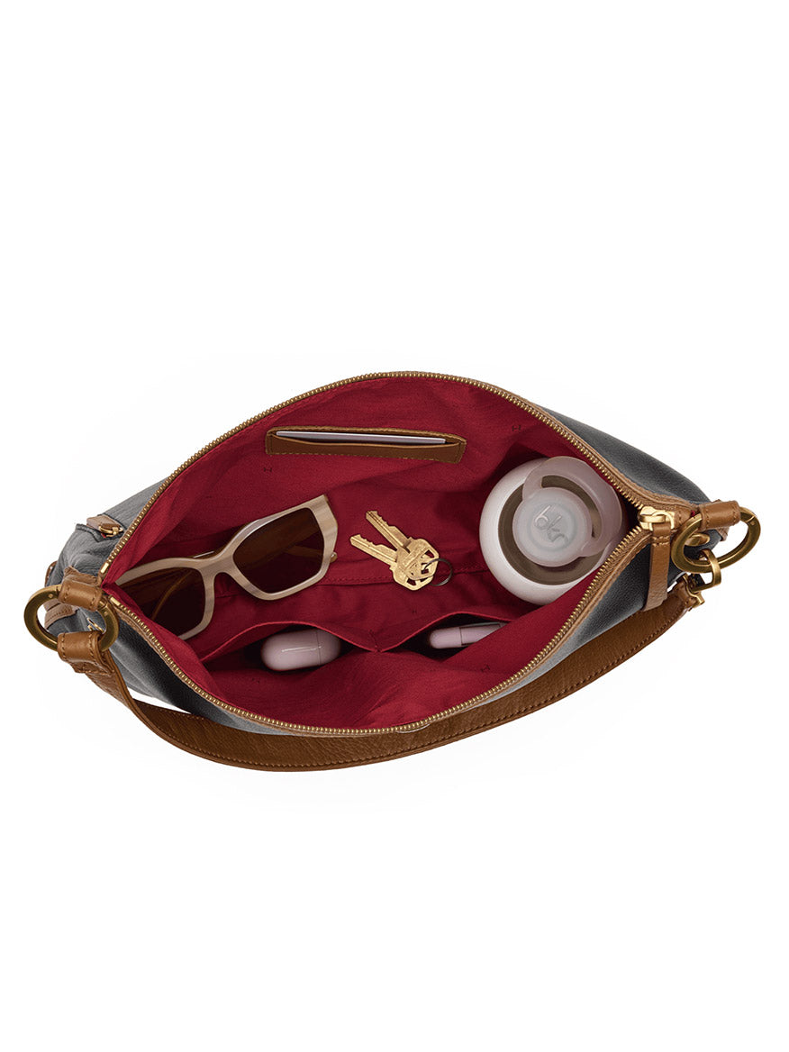 A Hammitt Los Angeles Kyle Large Shoulder Bag in East End/Antique Gold, crafted from black pebbled leather with a red interior, sits open to reveal sunglasses, a set of keys, a small container, and two lipsticks inside.