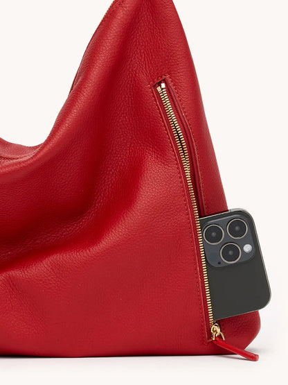 A black smartphone peeks from the zippered pocket of the Hammitt Los Angeles Kyle Large Shoulder Bag in Chili Red/Gold.