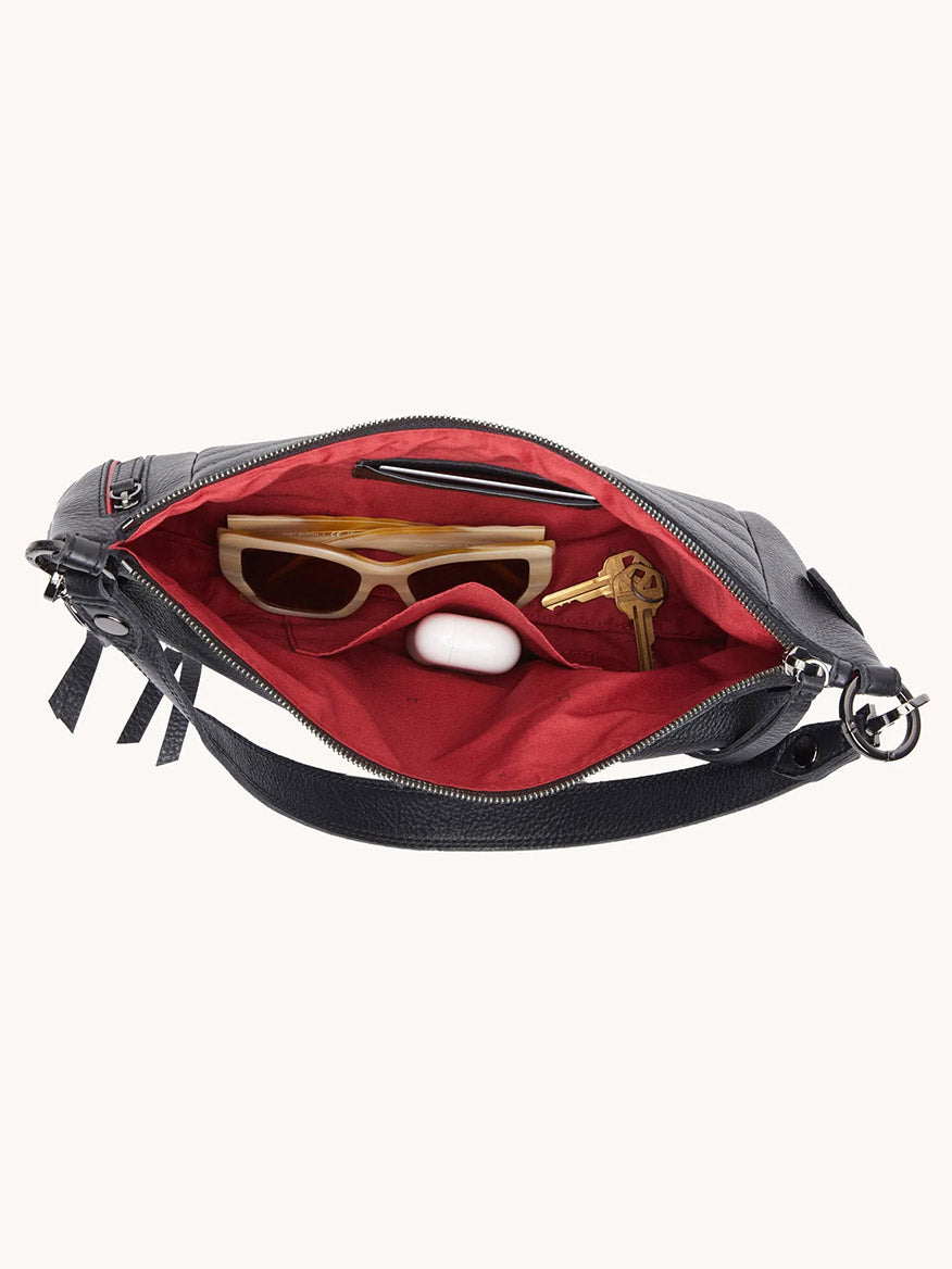 A Hammitt Los Angeles Kyle Medium Shoulder Bag in Moto Black/Gunmetal with a red interior holds sunglasses, keys, and wireless earbuds.