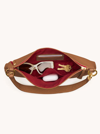 The Hammitt Los Angeles Kyle Medium Shoulder Bag in Mahogany Pebble/Brushed Gold & Red Zip is open, revealing sunglasses, a white case, keys, and a wallet organized inside its red interior.