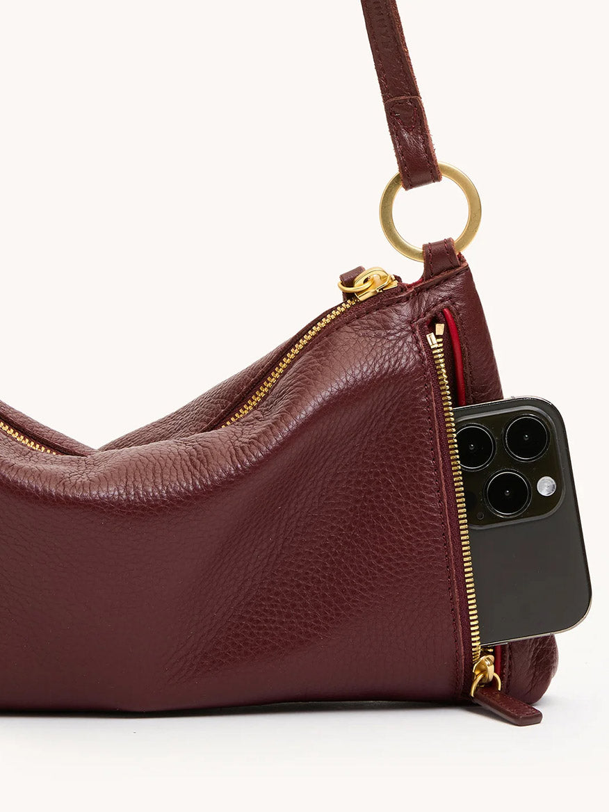 The Hammitt Los Angeles Kyle Shoulder Bag in Cherrywood Pebble/Brushed Gold has a gold zipper and an exterior pocket, partially open to show a black smartphone inside.