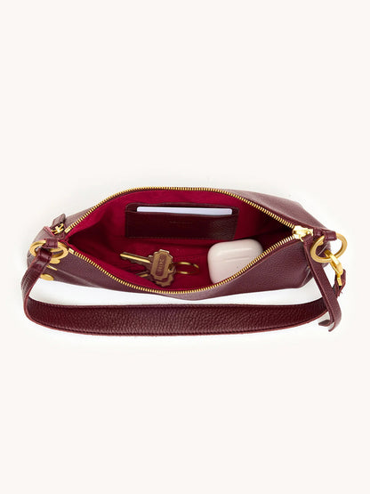 The Hammitt Los Angeles Kyle Shoulder Bag in Cherrywood Pebble/Brushed Gold features an adjustable crossbody strap, gold zipper, and red lining. Shown open with a phone, key, and white case inside.