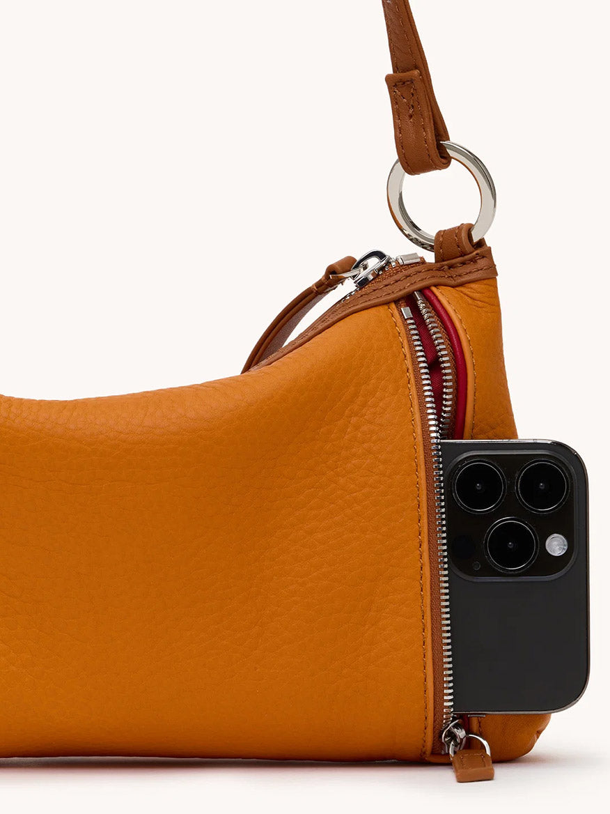 The Hammitt Los Angeles Kyle Shoulder Bag in Tailored Tangerine/Silver features a partially open metal zipper, with a black smartphone visible inside the front pocket.