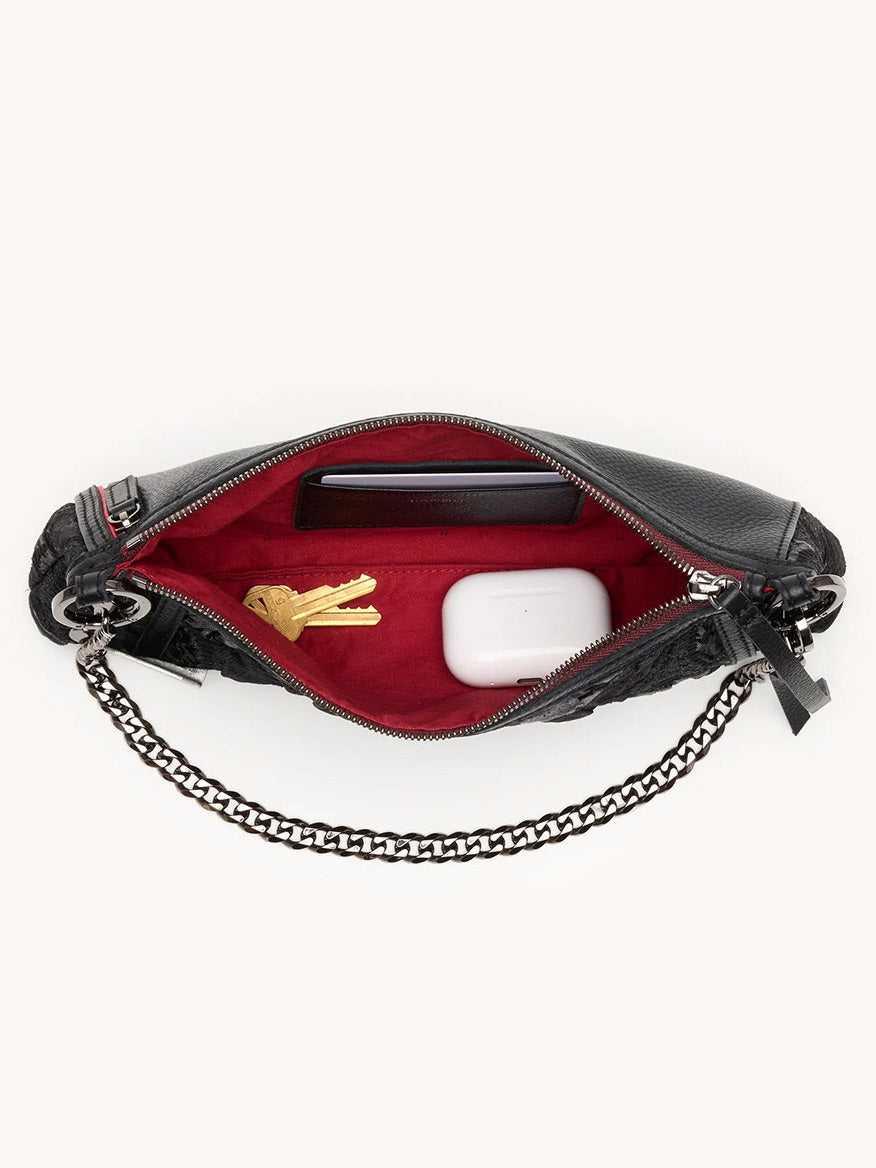 The Hammitt Los Angeles Kyle Shoulder Bag in Midnight Marquise/Gunmetal, unzipped to reveal a red interior, holds keys, a phone, and wireless earbuds in a case.