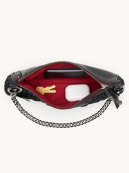 The Hammitt Los Angeles Kyle Shoulder Bag in Midnight Marquise/Gunmetal, unzipped to reveal a red interior, holds keys, a phone, and wireless earbuds in a case.