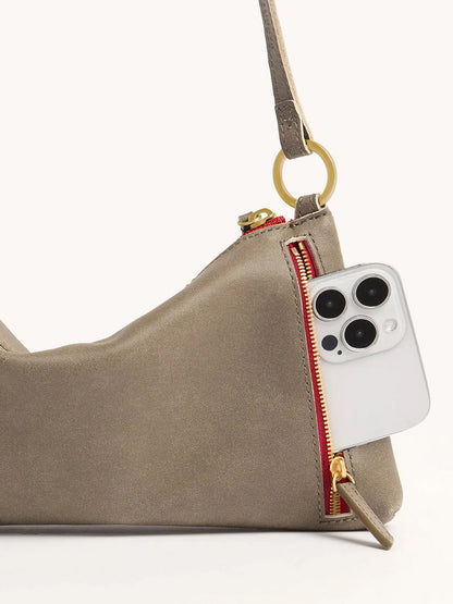 A Hammitt Los Angeles Kyle Shoulder Bag in Pewter with brushed gold hardware and a red zip, partially open, holding a white smartphone.