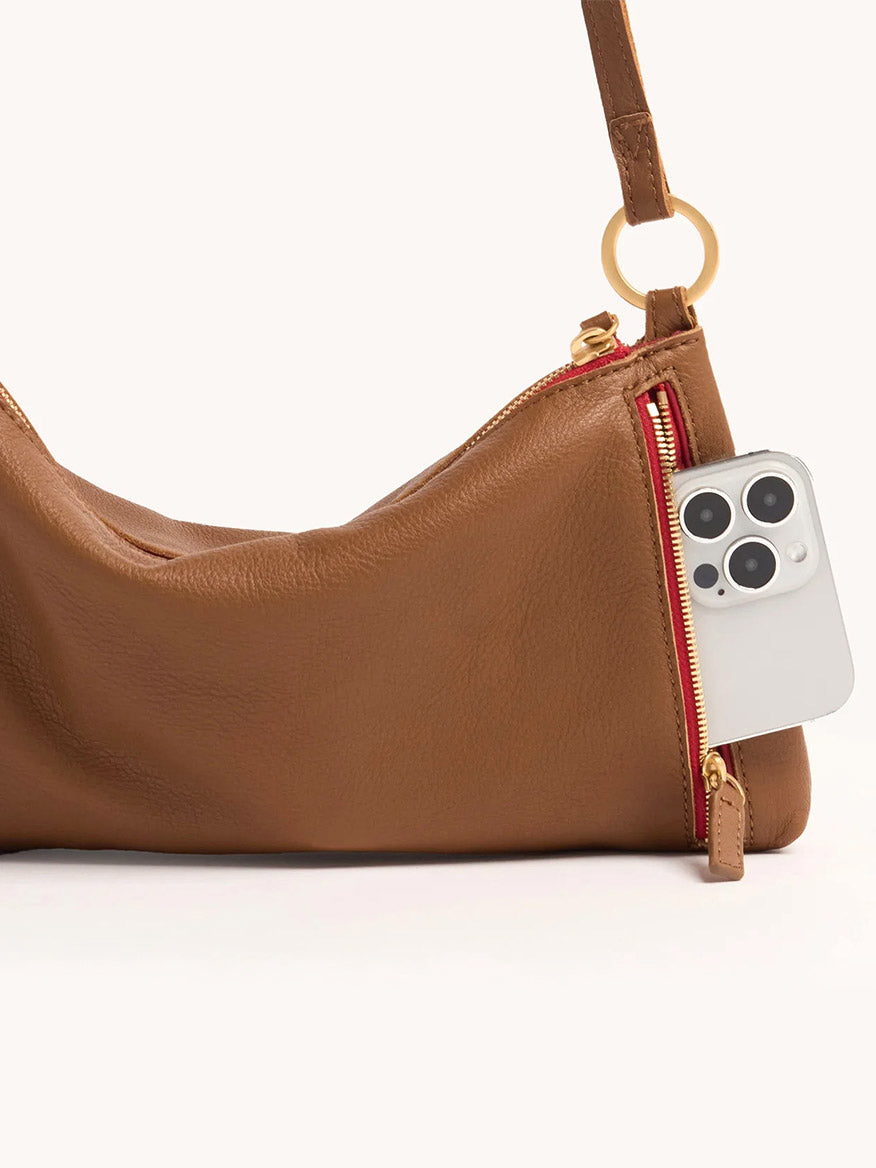 The Hammitt Los Angeles Kyle Shoulder Bag in Mahogany Pebble & Red Zip features a gold ring detail and a side zip pocket, which is partially unzipped to reveal a smartphone inside.