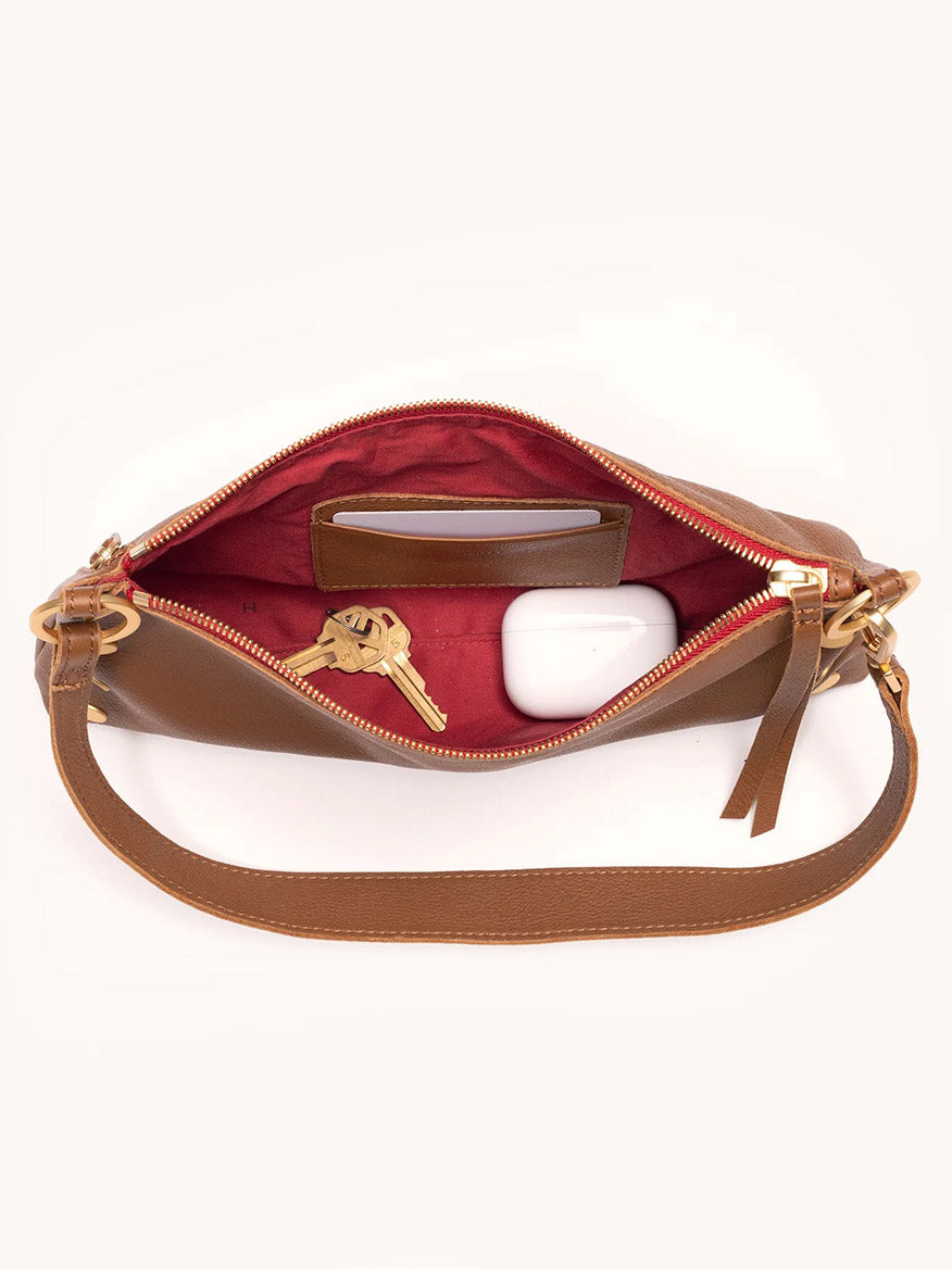 The Hammitt Los Angeles Kyle Shoulder Bag in Mahogany Pebble & Red Zip is unzipped, revealing keys, a white case, and a card inside its rich red interior.