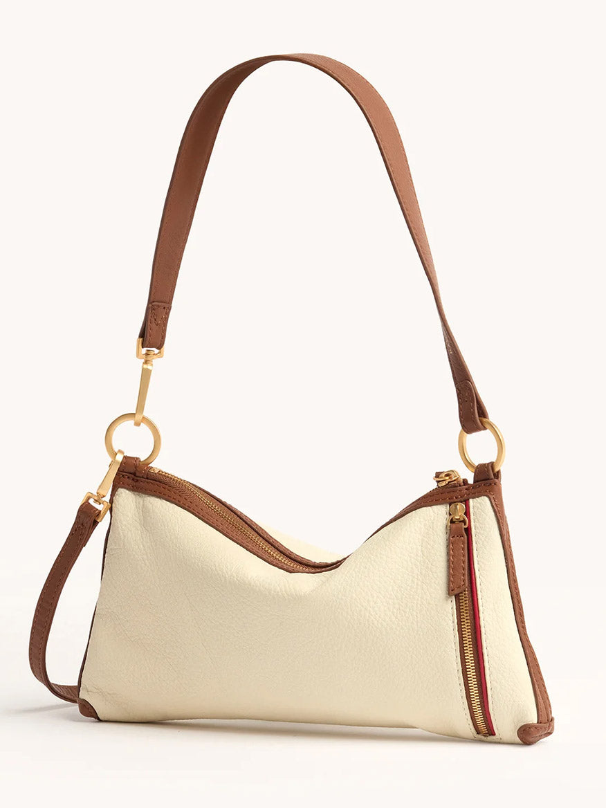 The Hammitt Los Angeles Kyle Shoulder Bag in Courtyard Cream features cream pebbled leather, brown accents, a gold zipper, a side pocket with red zipper, and a brown adjustable crossbody strap.