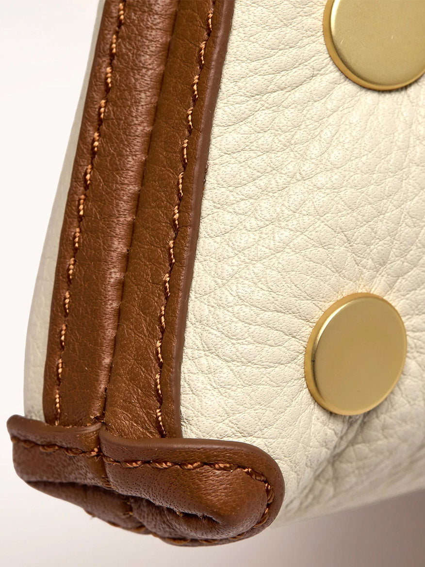 Close-up of the Hammitt Los Angeles Kyle Shoulder Bag in Courtyard Cream, featuring beige pebbled leather, brown leather trim, gold round studs, and an attached crossbody strap.