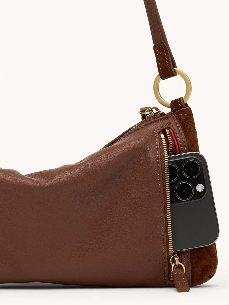 The Hammitt Los Angeles Kyle Shoulder Bag in Chocolate Diamond Suede/Antique Gold features a gold zipper pocket, shown partially unzipped with a black smartphone inside.