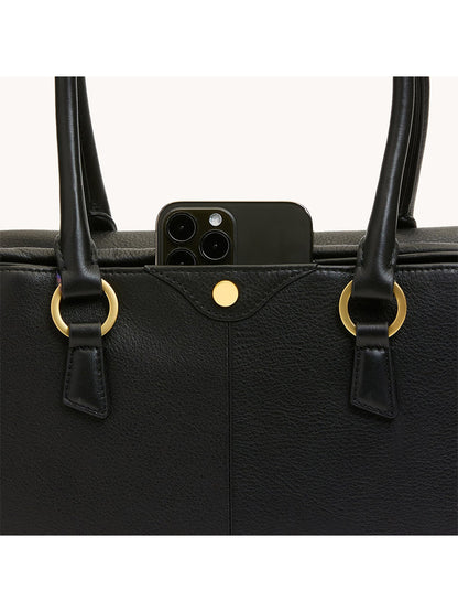 A black smartphone peeks from the outer pocket of the Hammitt Los Angeles Meredith Medium in Black/Brushed Gold, featuring gold hardware and double handles that enhance its chic, doctor-style bowling bag silhouette.