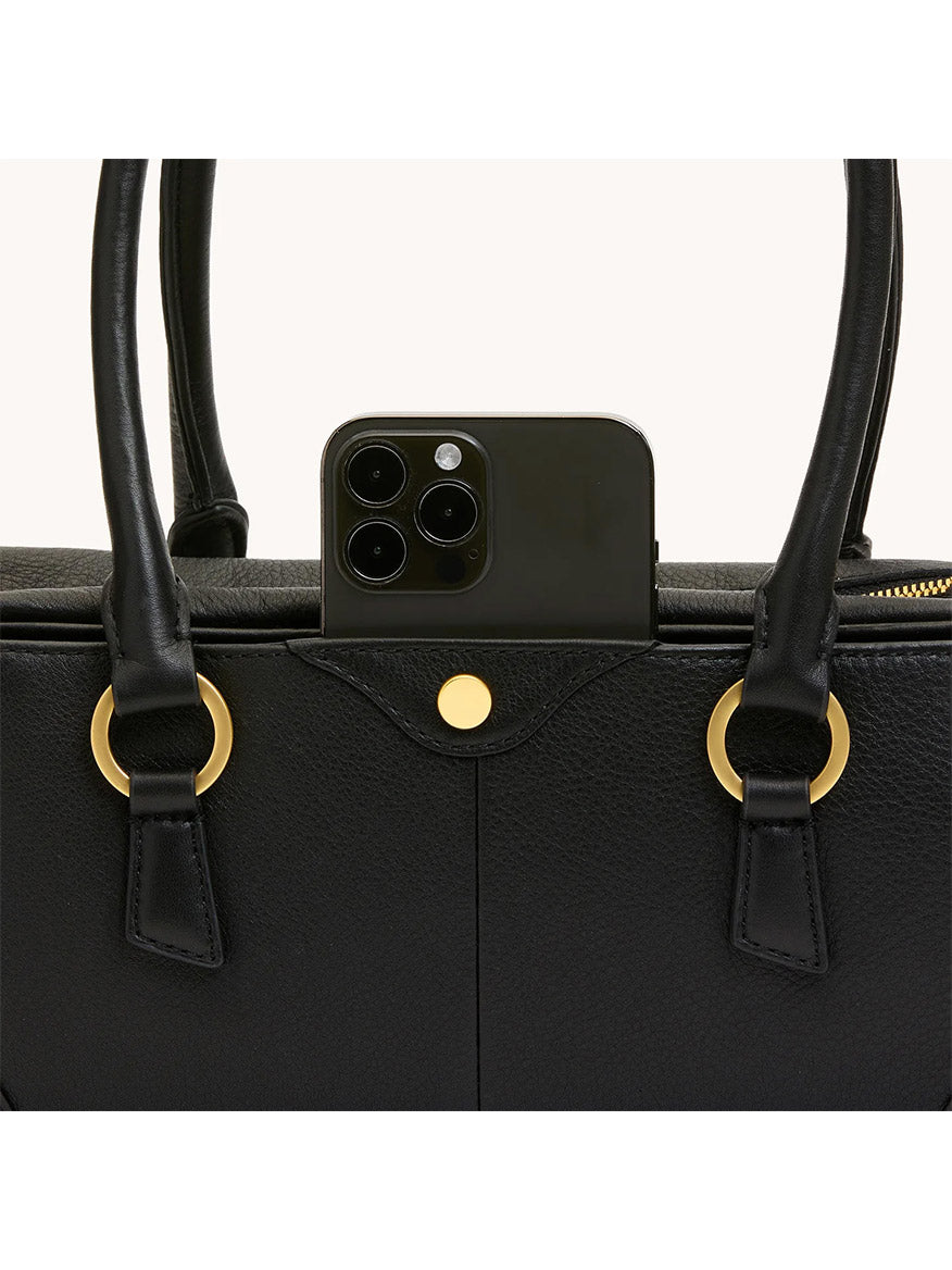 A black smartphone is partially inserted into an exterior pocket of the Hammitt Los Angeles Meredith Small in Black/Brushed Gold handbag.